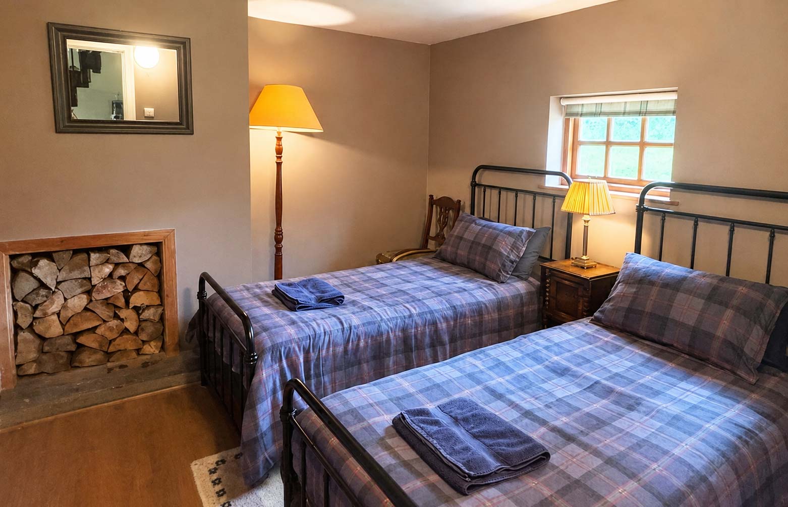 A twin bedroom in the Bothy at Glen Dessary with tartan bedding and a log store